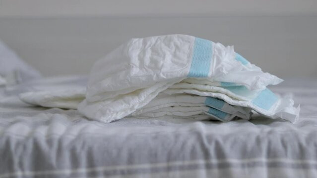 baby stack many diapers on bed woman mother hand taking one or pressing push with palm.white empty diaper throwing on bed slow motion maternity child infant new born toddler care concept