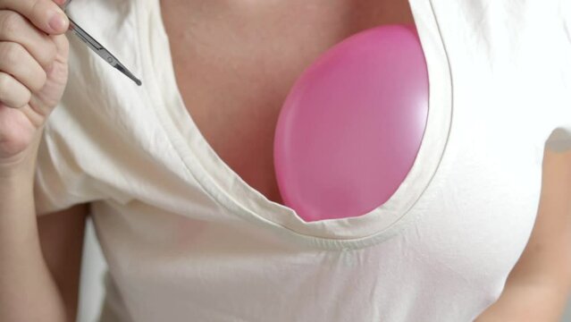 woman holding two pink purple inflatable balloon at breast dancing doing some moves with body.hand with scissors breaks the balloon video slow motion