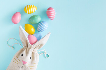 Flat lay cloth bag rabbit with easter eggs on a pastel blue background with copy space top view