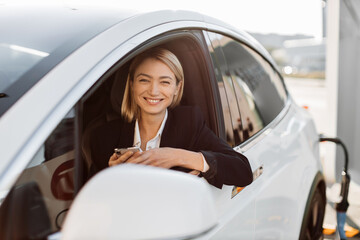 Attractive caucasian woman with modern smartphone in hands sitting inside luxury car while...