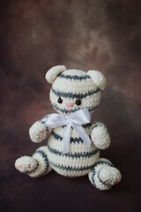 a small knitted white with black stripes kitten with a long thin tail and a white butterfly on its neck sits on a beautiful background