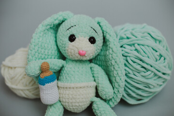 cute knitted light green bunny with big ears in a white diaper with a knitted white pacifier with two skeins of white and light green knitting yarn