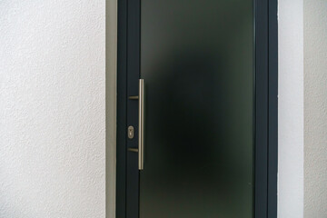 A closed glass door inside an office or cafe. Interior design, black metal door on a white wall background. Evacuation exit from the building during a fire or other cataclysm. Emergency fire exit