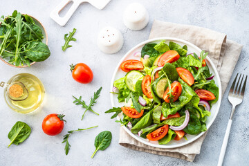 Fresh green salad with leaves, vegetables and olive oil. Top view at light stone table.