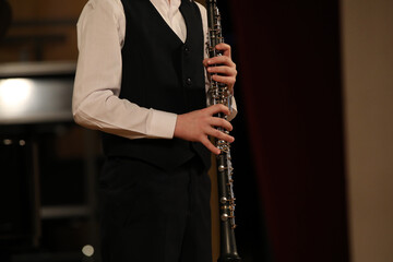 A young clarinetist musician stands with a musical instrument in his hands