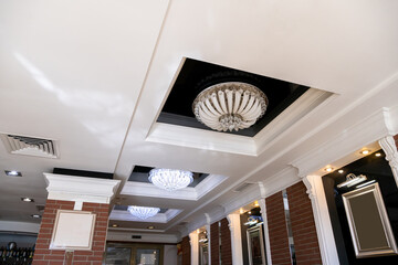 Elegant crystal chandeliers hang on the white ceiling in the lobby of the restaurant. Modern diode...