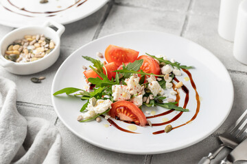 Healthy vegetable salad with fresh arugula, tomato, feta cheese on white plate with cutlery, gray tile background. Diet menu. Appetizer salad