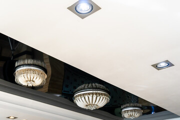 Elegant crystal chandeliers hang on the white ceiling in the lobby of the restaurant. Modern diode...