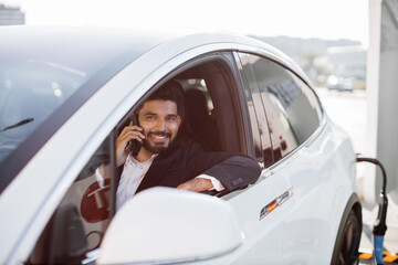 Attractive bearded man in formal suit talking on smartphone while sitting inside brand new auto....