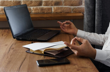 A businessman meditates while working on a laptop, sitting with his eyes closed at his workplace in a home interior.