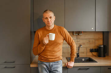 Portrait of a mature man in an orange jumper in the kitchen with a mug of warm tea