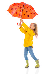 Seven years old blonde hair girl in yellow raincoat posinп in studio with umbrella. Full-length portrait of cute child isolated on white background.