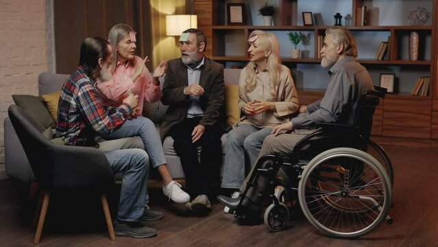 Group of Senior Friends in an Elite Nursing Home Playing Funny Game Who I Am. Smiling Elderly Players Sitting at the Table with Paper Stickers. Old People Spending Time Together, Enjoying the Game