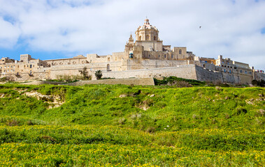 Fototapeta na wymiar Fortified city called Mdina Maltese L-Imdina in Malta, Europe. City seen from outside of fort and walls, lush green fields around the city medieval walls.