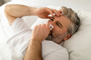 Closeup of sick middle aged man sneezing in bed