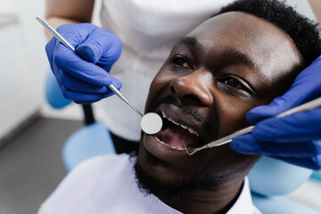 Consultation with dentist at dentistry. Teeth treatment. Dentist examines african man mouth and...