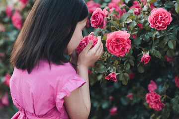 Kid girl 4-5 year old smelling pink rose flowers in garden over nature background outdoor. Springtime. Childhood.