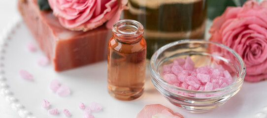 Aromatherapy. Pure organic essential rose oil concept. Elixir with plant based floral herbal ingredients. Pink flowers extract. Spa atmosphere with candle, towel. White background. Banner copy space