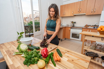 Athletic girl in sportswear cooking in a kitchen with fresh vegetables, vegan or vegetarian woman. Proper nutrition concept