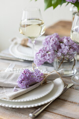 Obraz na płótnie Canvas Beautiful table decor for a wedding dinner with a spring blooming lilac flowers. Celebration of a special holiday marriage event. Fancy white plates, wineglasses. Countryside style