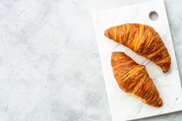 Croissant on cutting board at white table top view. French bakery.