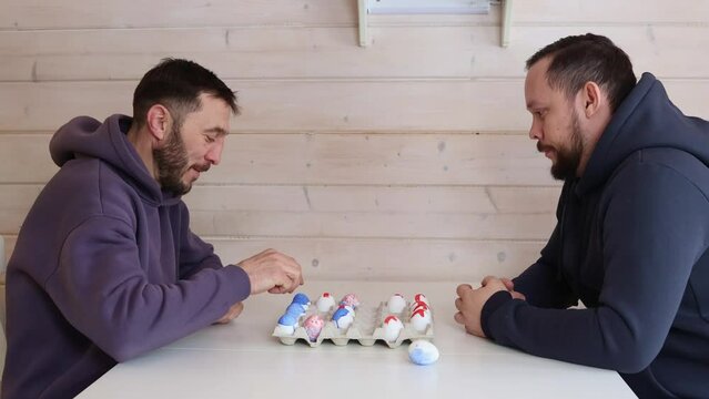 Bearded men play chess with Easter eggs at white table. Creative ideas for unusual chess. Colorful painted egg figures. High quality 4k footage