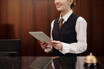 Close-up of young woman in uniform of receptionist holding tablet while standing by workplace in...