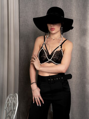 sexy woman.She has a beautiful, slim figure. She wears a black bra and a pearl necklace and a black hat.