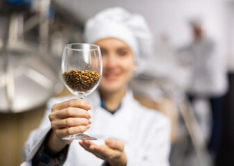Portrait of positive female brewer with a glass of barley at the brewery