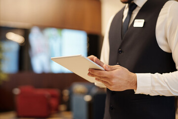 Close-up of young elegant male receptionist using tablet while standing in front of camera in...