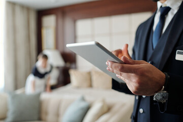 Close-up of young male manager of hotel using digital tablet while looking through list of booked...