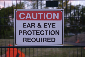 Sign caution ear and eye protection required on the metal fence at construction site.  Workplace hazards and safety concept. Selective focus.