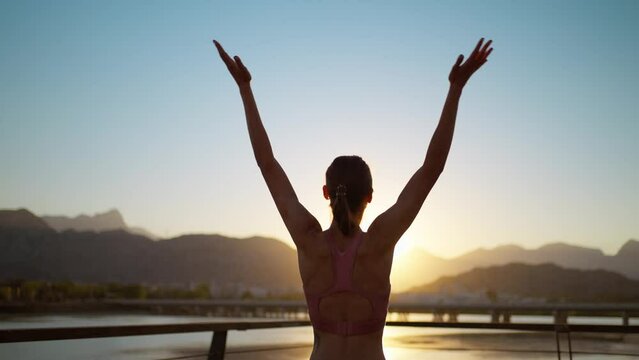 Rear view silhouette sporty woman standing on bridge with hands up in Tree Yoga Pose. Practicing yoga during sunset with nature view