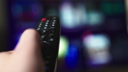 Mans hand selects internet tv channels with remote control, close-up. Person controls TV using a...