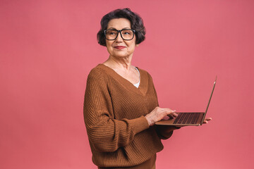 Senior aged business woman with laptop. Grandmother isolated over pink background.