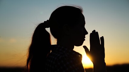 Silhouette Young woman praying at sunset. Christian prayer in nature. Morning prayer of girl...