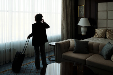Rear view of businesswoman talking on smartphone while standing in front of large window covered...