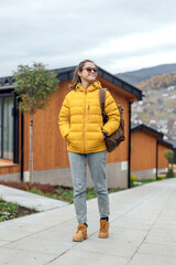 Young female in yellow down jacket walks outdoor near modular cabin houses