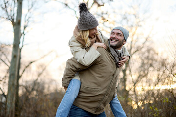 A handsome man giving his girlfriend a piggyback ride outdoors