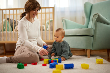 Mother and her baby boy playing with colored toy blocks at home