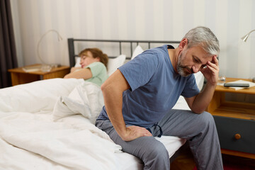 Mature man looking worried while his wife sleeps in the background