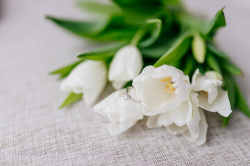 An engagement ring in white gold with a diamond lies in a bouquet of white tulips.  Gift for...