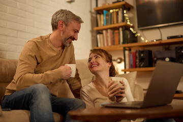 Fototapeta premium Happy mature couple enjoying their coffee time in the living room using laptop