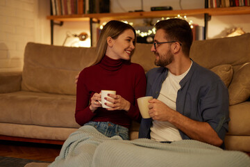 Obraz premium Young couple drinking tea while sitting in the living room at night