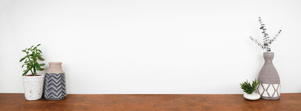 Home decor and plant on a shelf. Clay vases and succulent plants on a wood shelf against a white wall. Banner with copy space.