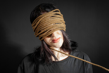 Portrait of a poor skinny girl in black crumpled clothes with a rope wrapped around her head and...