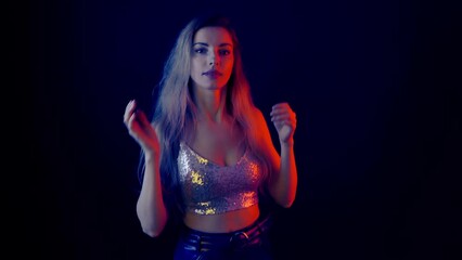 Young woman dancing in party fashionable shiny outfit. Smiling excited sexy lady dance waving hands moving on camera having fun in neon light listening to music at a nightclub, party