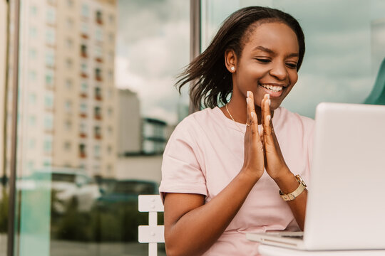 Happy african american woman hipster clapping hands sitting outside with laptop, excited triumph euphoric winner. Young entrepreneur freelancer student businesswoman, sale offer discount lottery
