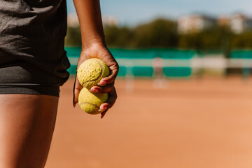 African american woman hold yellow green balls, playing tennis match on clay court surface on weekend free time sunny day. Female player ready to serve. Professional sport concept

 - obrazy, fototapety, plakaty