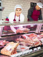 Successful young female butcher shop worker preparing meat products for sale in glass fridge...